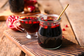 Jar and gravy-boat of pomegranate molasses on wooden background