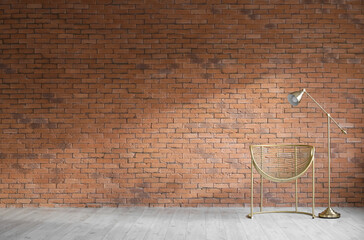 Modern armchair and standard lamp near brick wall