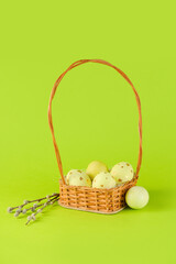 Wicker basket of painted Easter eggs and pussy willow on green background