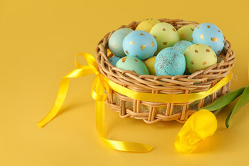 Wicker basket of painted Easter eggs and flowers on yellow background