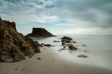 long exposure of a picturesque small beach in a rocky cove with reef at low tide