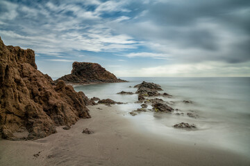 long exposure of a picturesque small beach in a rocky cove with reef at low tide