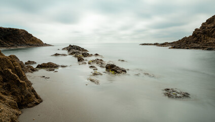 long exposure of a picturesque small beach in a rocky cove with reef at low tide