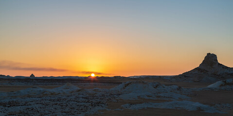 Wind eroded rock formations in the background of sun going down and sunset, Egyptian White Desert....