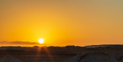 Fototapeta na wymiar Sun going down and orange sky, wind eroded rock formations, Egyptian White Desert. Western Desert, Egypt