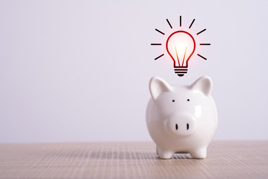 saving energy economy and money concept. creative idea for save or investment. piggy bank on desk with light bulb icon planning money finance. Copy space for text.