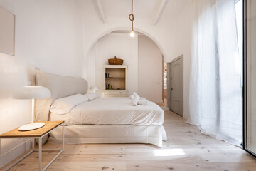 Nice bedroom with a king size bed, light pine wood floors, white curtains and a semicircular chest on one side of a room