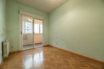 Empty living room with oak herringbone parquet flooring, light green walls and bay window with exit to terrace