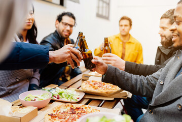 multiracial group of friends toasting with beer during the celebration of a meal on a terrace. Female and male co-workers eating after workday