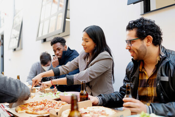 Diverse, multiracial group of friends eating pizza and drinking beer together outdoors. Celebrating friendship together.