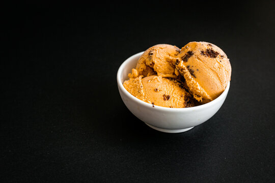 Pumpkin ice cream with brownie chunks in a white cup on the black background