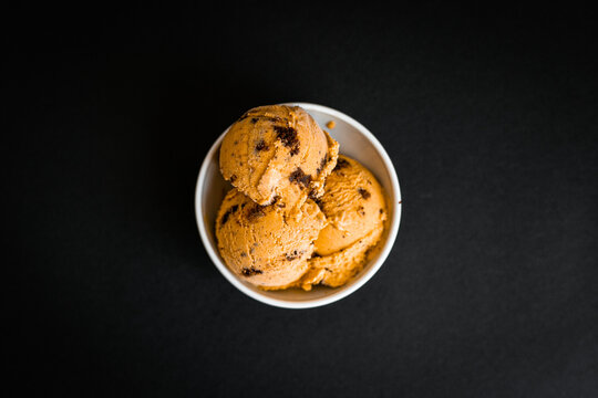 Pumpkin ice cream with brownie chunks in a white cup on the black background shot from the top