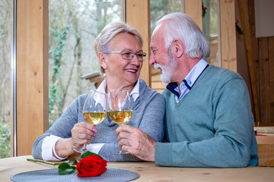 A Mature Romantic Couple Of Caucasian Man And Woman Sit In A Restaurant. Seniors In Love, Looking At Each Other, Drink, Toast And Clink Glasses With Wine.