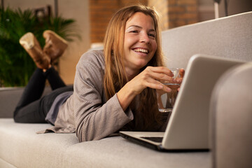 Fototapeta na wymiar Girl holding a glass of water. Smiling girl drinking water while using the laptop.