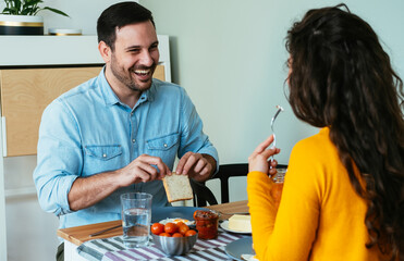 Happy Couple Laughing Together While Eating Breakfast at Home. 
Smiling man talking to unrecognizable woman while having breakfast together in the dining room.