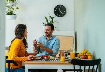 Happy Couple Eating Breakfast Together at Home. 
Smiling husband feeding his wife and sharing meal while sitting at kitchen table.