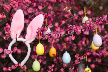 Stylish background with colorful easter eggs hanging on blooming plum tree branches outdoor in park or garden