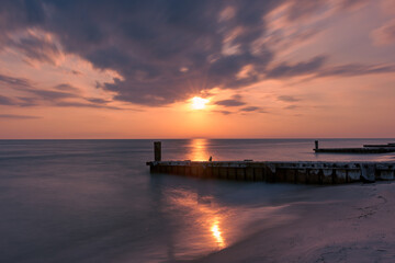 Sunset on the beach with the breakwater or jetty - obrazy, fototapety, plakaty