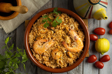 aerial photo of a clay dish with yellow rice with shrimp or Spanish paella accompanied by tomatoes, oil can and wooden mortar