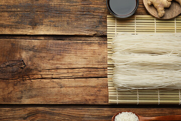 Flat lay composition with uncooked rice noodles, soy sauce and ginger on wooden table. Space for text
