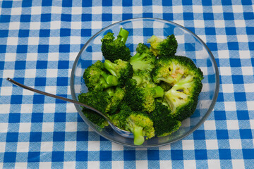 Boiled broccoli in a glass plate with a spoon on the table.