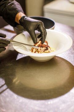mani da cuoco con guanti neri preparano un antipasto con un polpo e cremina di patate