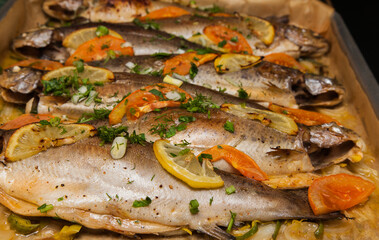 Fototapeta na wymiar Baked trout fish with slices of lemon, tomatoes, onions, dill and parsley in spices on a tray close-up.