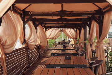 Cozy terrace of outdoor cafe with wooden furniture and beautiful curtains on windy day