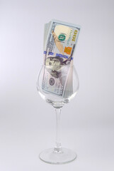 Fototapeta na wymiar Wine glass with US dollars banknotes on white background