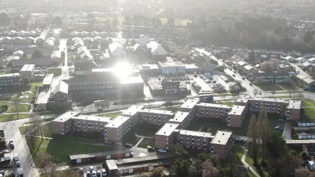 Aerial video of a double deck bus travelling past houses and apartments in bright reflected sunlight after a rain shower