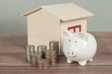 Piggy bank with the coins arranged in an orderly manner. Ideas to collect money for borrowing to buy a home in future, real estate. and wooden house model on white background on wooden table with copy