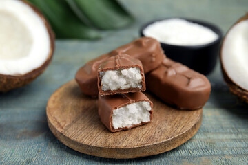 Delicious milk chocolate candy bars with coconut filling on blue wooden table, closeup