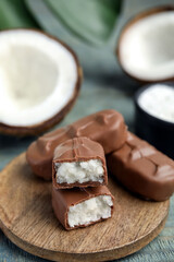 Delicious milk chocolate candy bars with coconut filling on blue wooden table, closeup. Space for text