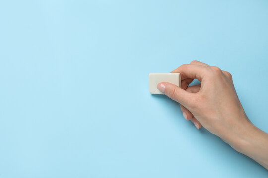 Woman erasing something on light blue background, closeup. Space for text