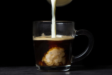 Cream is poured into coffee on a black background. Tonic coffee drink. Coffee with milk	