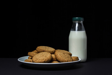 Oatmeal cookies with a bottle of milk on a black background. Light and tasty dessert. Healthy breakfast