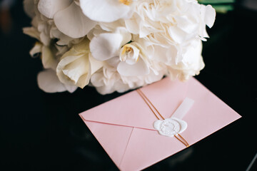 Beautiful wedding bouquet of white orchids and a pink envelope with a wedding invitation