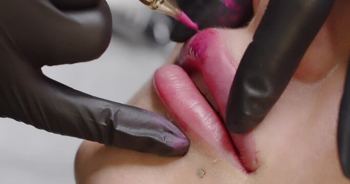 The master makes a lip tattoo for a client in a beauty salon with a special device