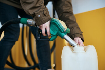 Close-up of woman filling plastic gallon with fuel at gas station.