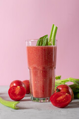 Healthy diet smoothie from celery and tomato in a tall glass on a pink background, vertical format