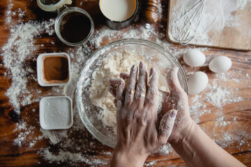 The process of making baking dough in a glass bowl on a wooden table sprinkled with flour. In the...