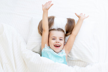 a little girl child woke up in the morning at home on a bed on a white cotton bed and yawns with her mouth