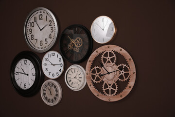Collection of stylish clocks on brown wall