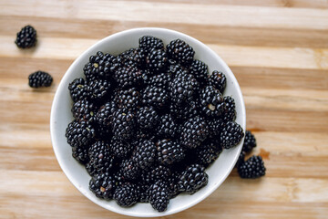 Blackberries in a white deep plate and on a wooden surface. Blackberry. Blackberry fruits close-up on a wooden table. View from above
