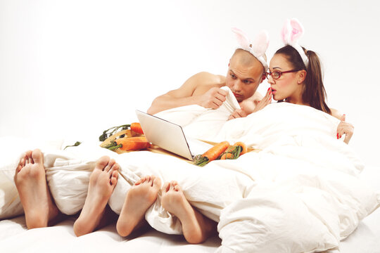 Lovely couple in rabbit costumes lying on bed and watching laptop