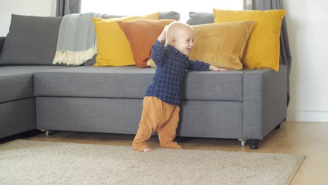 Family and children concept. Cute baby toddler holding on sofa learning how to stand on his legs