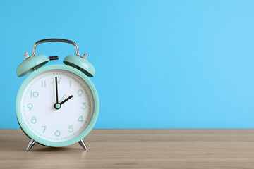 Turquoise alarm clock on wooden table against light blue background, space for text
