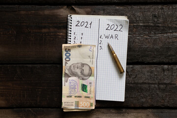 Notepad with the text of the year 2021 and 2022 next to the Ukrainian money and a bullet. Plans for the year 2022 war in Ukraine. All forces to win the war