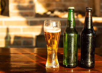 Empty glass and two bottle of beer on wooden table. Happy hour, golden sunset light illuminates the outdor patio.