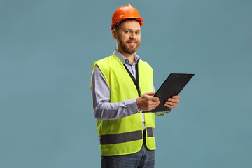 Site engineer wearing a reflective vest and helmet holding a clipboard and looking at camera